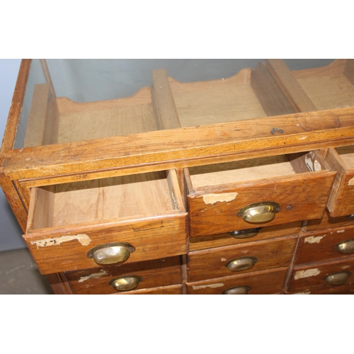 81 - An early 20th century light oak haberdashery shop counter or display cabinet with 30 drawers with br... 