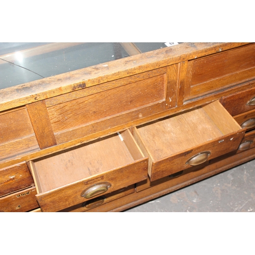 82 - An early 20th century light oak haberdashery shop counter or display cabinet with 15 drawers with br... 