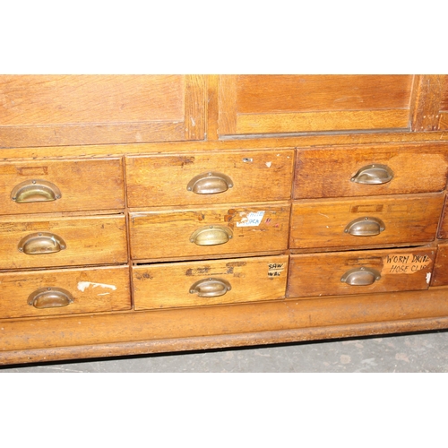 82 - An early 20th century light oak haberdashery shop counter or display cabinet with 15 drawers with br... 