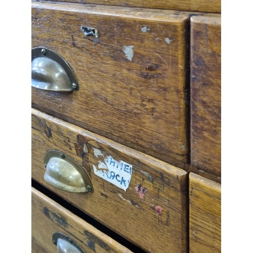 82 - An early 20th century light oak haberdashery shop counter or display cabinet with 15 drawers with br... 