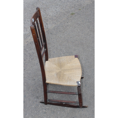 20 - An Arts & Crafts period rush seated rocking chair in the manner of Liberty, with bobbin turned stret... 