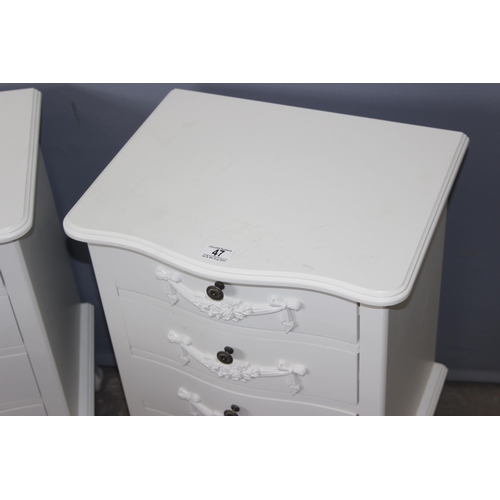 47 - A pair of vintage style white painted 4 drawer bedside cabinets with decorative floral swags and met... 