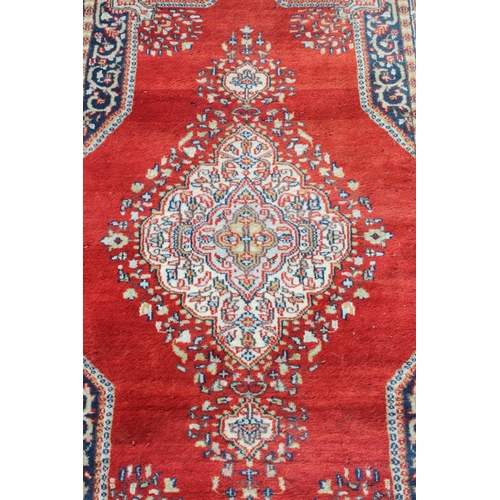 200 - A vintage hand made red ground rug with decorative cream medallion centre, approx 156cm x 87cm