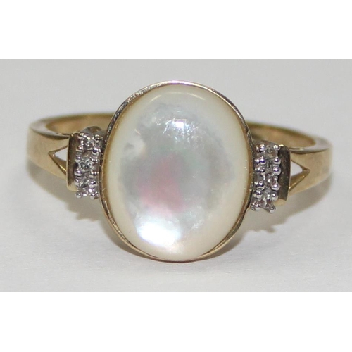 2063 - A 9ct gold oval shaped mother of pearl cabochon ring flanked by small diamonds, full English hallmar... 