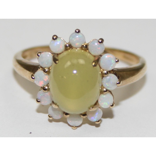 2069 - A 9ct gold dress ring, a central cloudy green cabochon stone surrounded by 12 small opals, full Engl... 