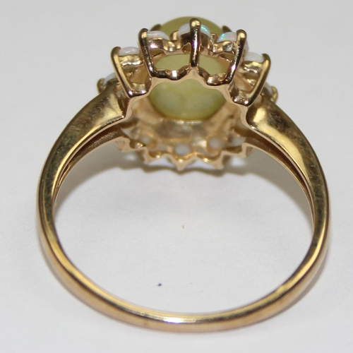 2069 - A 9ct gold dress ring, a central cloudy green cabochon stone surrounded by 12 small opals, full Engl... 