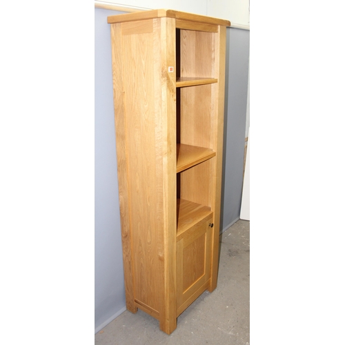 29 - A tall slim modern light oak bookcase with cupboard, likely from Oak Furnitureland, approx 63cm wide... 