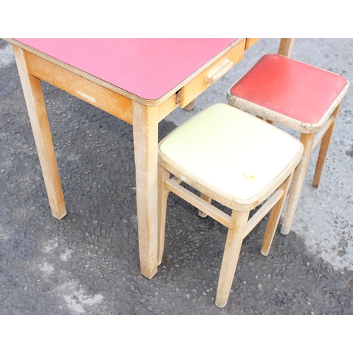 54 - A small mid-century Formica topped table with small drop flap and 2 drawers, and retro stools, the t... 