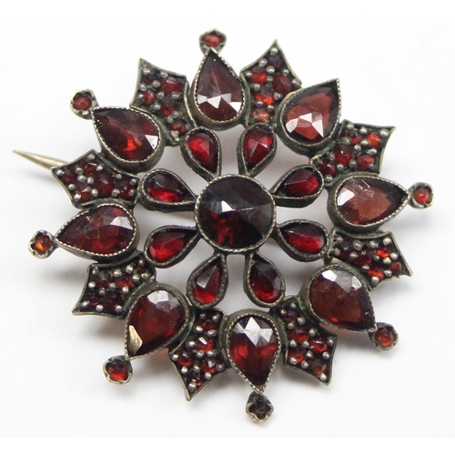 1146 - A Georgian style star shaped Garnet cluster brooch comprised of three tiers of mixed cut garnets in ... 