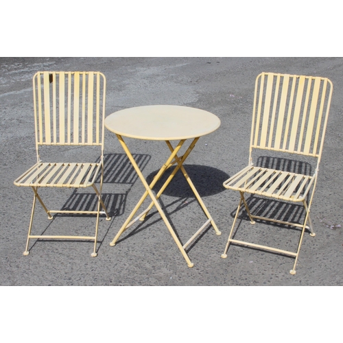 317 - A small faded yellow painted metal bistro set with 2 folding chairs and a table, approx 62cm wide x ... 