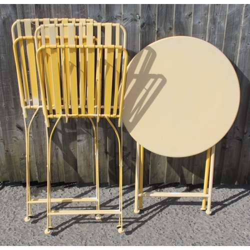 317 - A small faded yellow painted metal bistro set with 2 folding chairs and a table, approx 62cm wide x ... 