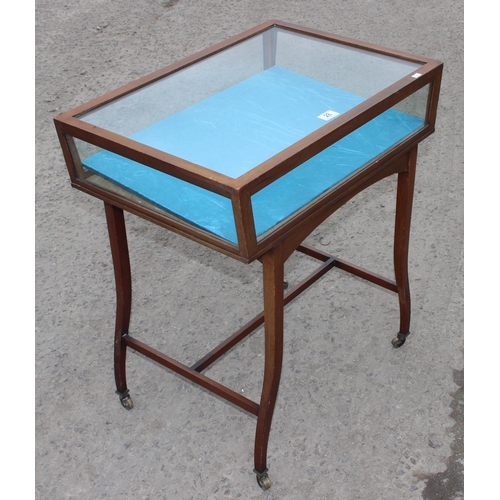 28 - A vintage glazed mahogany bijouterie table with thin legs and castors, approx 66cm wide x 47cm deep ... 