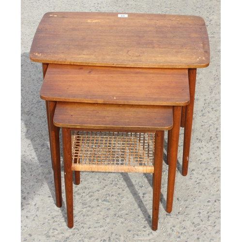 69 - A retro teak nest of 3 tables, the smallest with rattan magazine rack, strongly in the manner of Dan... 