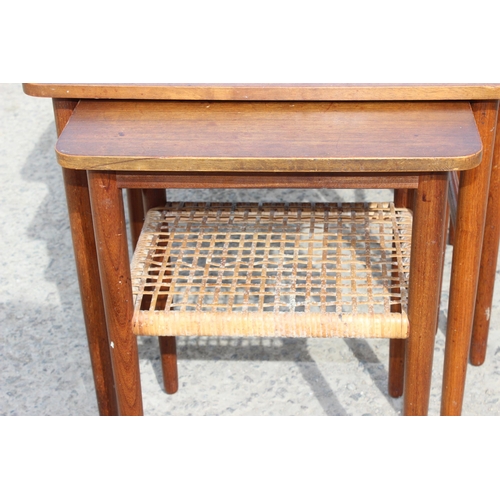 69 - A retro teak nest of 3 tables, the smallest with rattan magazine rack, strongly in the manner of Dan... 