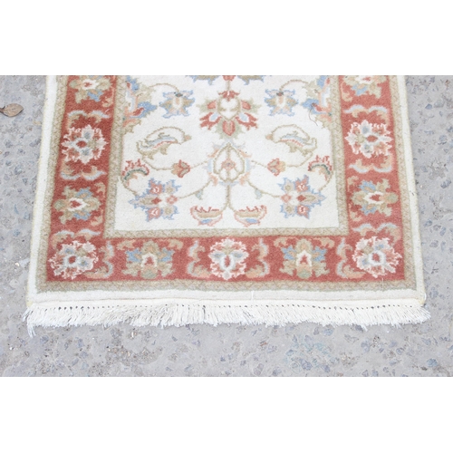 214 - A vintage hand made cream ground runner rug with decorative red border, approx 180cm wide x 62cm dee... 