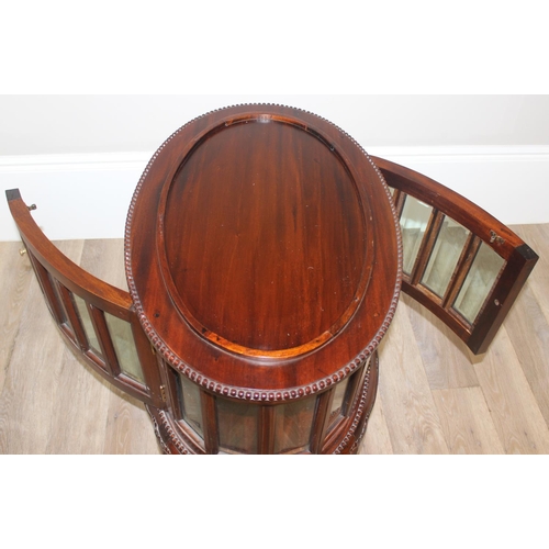 25 - A 20th century mahogany drinks cabinet of oval form with tray top above a glazed door and sides on s... 