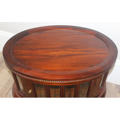 25 - A 20th century mahogany drinks cabinet of oval form with tray top above a glazed door and sides on s... 