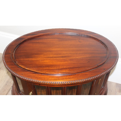 25 - A 20th century mahogany drinks cabinet of oval form with tray top above a glazed door and sides on s... 