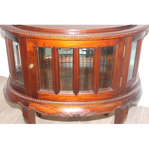 25 - A 20th century mahogany drinks cabinet of oval form with tray top above a glazed door and sides on s... 