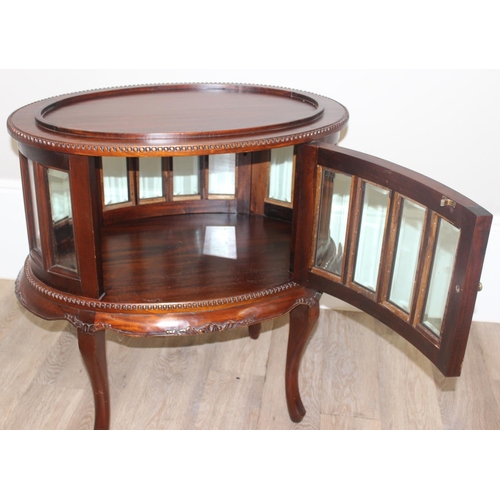 25 - A 20th century mahogany drinks cabinet of oval form with tray top above a glazed door and sides on s... 