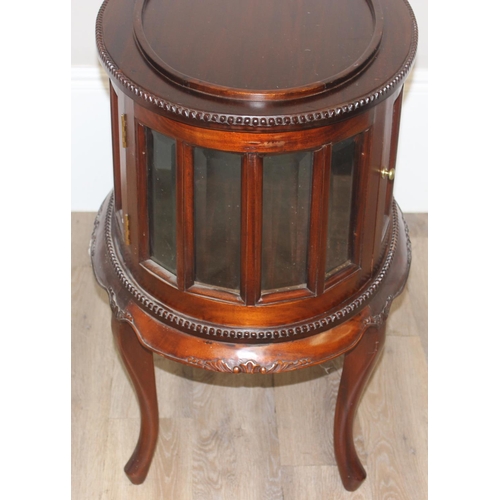 25 - A 20th century mahogany drinks cabinet of oval form with tray top above a glazed door and sides on s... 