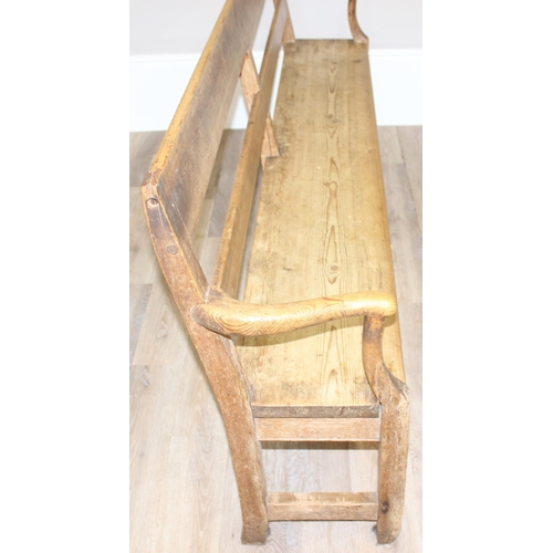 3 - An antique rustic pine bench with shaped arms and high back, likely 19th century, approx 205cm wide ... 