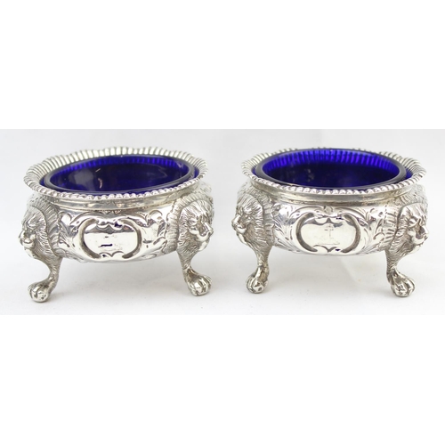 1048 - A pair of early Victorian cast silver salts with floral and lion head decoration, with blue glass li... 