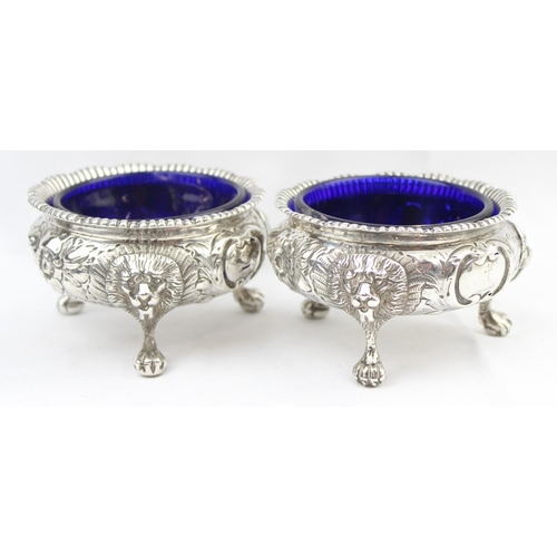 1048 - A pair of early Victorian cast silver salts with floral and lion head decoration, with blue glass li... 