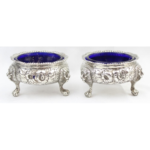 1048 - A pair of early Victorian cast silver salts with floral and lion head decoration, with blue glass li... 