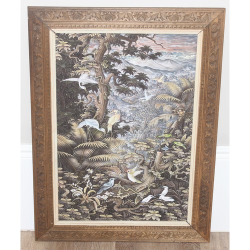 421 - Balinese School, painting on canvas of cranes within a forest setting, mounted in decorative carved ... 