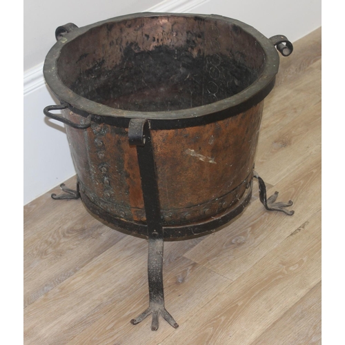 149 - A Victorian copper boiler with riveted join presented in a vintage blacksmith made wrought iron stan... 