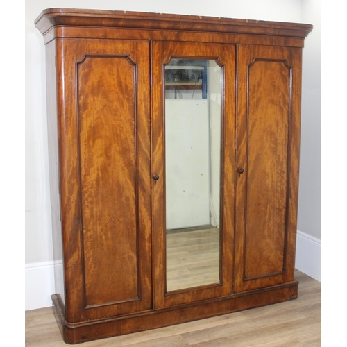 60 - A Victorian mahogany triple wardrobe press, the mirror and panel doors enclosing 4 trays, 2 over 2 d... 