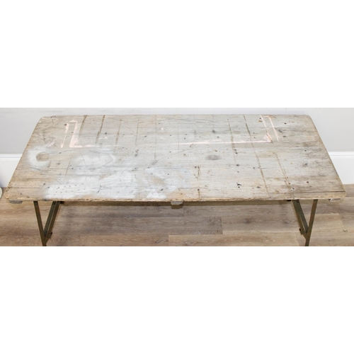 108A - A vintage weathered pine trestle table with folding metal legs, military markings to base and dated ... 