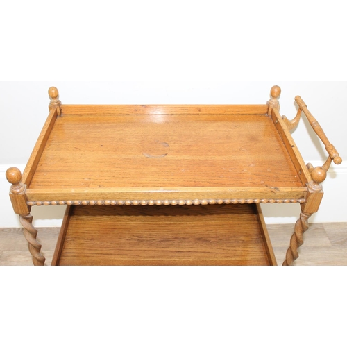 78 - A vintage oak serving trolley with barley-twist supports and wheels, approx 83cm wide x 46cm deep x ... 