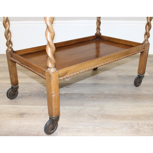 78 - A vintage oak serving trolley with barley-twist supports and wheels, approx 83cm wide x 46cm deep x ... 