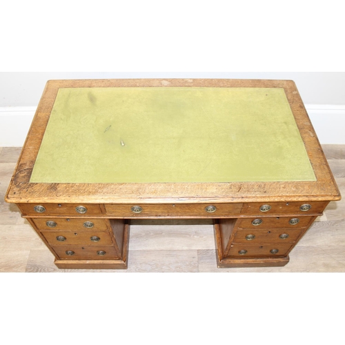 82 - An antique oak 9 drawer pedestal desk with green inset leather top and brass ring handles, early 20t... 