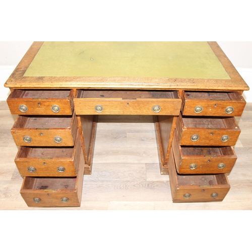 82 - An antique oak 9 drawer pedestal desk with green inset leather top and brass ring handles, early 20t... 