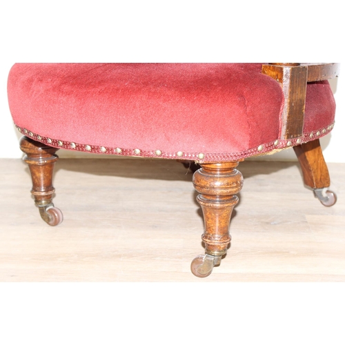 86 - A 19th century red button backed low armchair or library chair with turned wooden legs and scroll ba... 