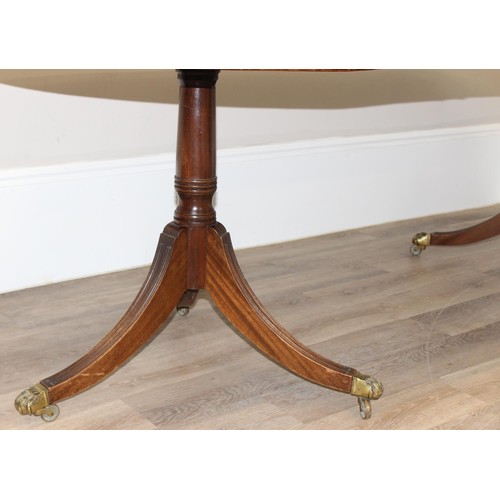 51 - An antique style mahogany twin pedestal dining table with extensions and brass lion paw castors, app... 