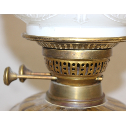 234 - An antique oil lamp with moulded milk glass shade, a glass reservoir, and an embossed brass base, ma... 