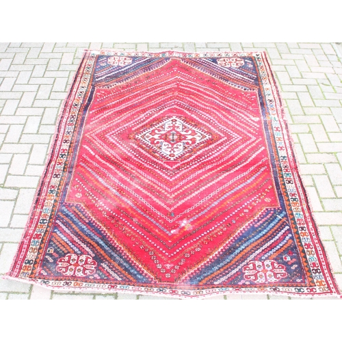 205 - A large vintage red ground rug decorated with a large geometric diamond pattern, possibly Caucasian,... 