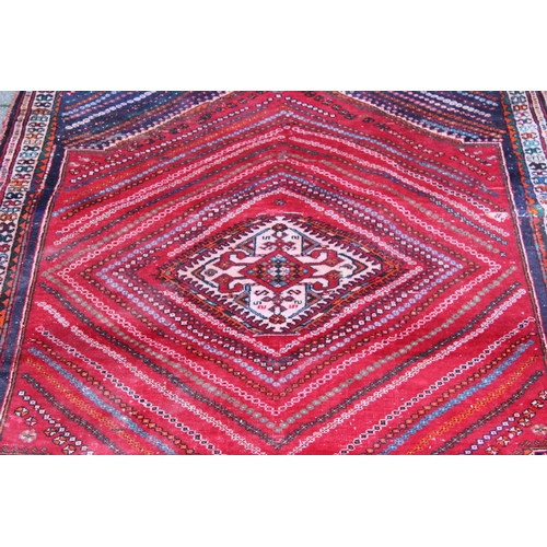 205 - A large vintage red ground rug decorated with a large geometric diamond pattern, possibly Caucasian,... 