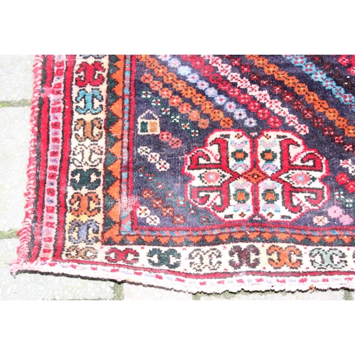 205 - A large vintage red ground rug decorated with a large geometric diamond pattern, possibly Caucasian,... 