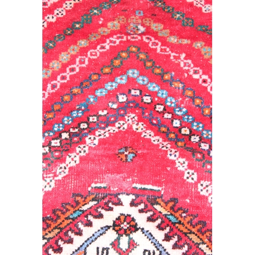 205 - A large vintage red ground rug decorated with a large geometric diamond pattern, possibly Caucasian,... 