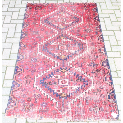 207 - A large vintage red ground rug with geometric patterns, worn, approx 200cm x 114cm