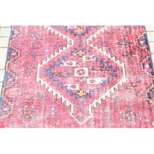 207 - A large vintage red ground rug with geometric patterns, worn, approx 200cm x 114cm