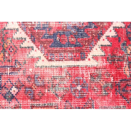 207 - A large vintage red ground rug with geometric patterns, worn, approx 200cm x 114cm