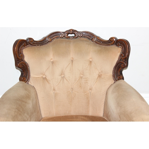 63 - An antique style button back low armchair with exposed carved wooden frame and gold upholstery, appr... 