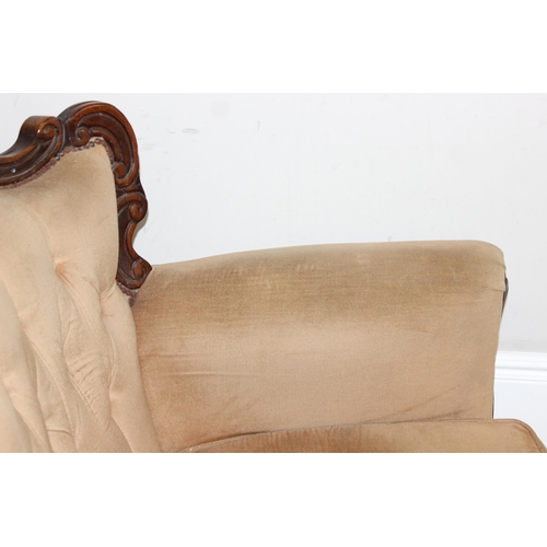 63 - An antique style button back low armchair with exposed carved wooden frame and gold upholstery, appr... 