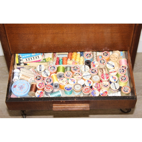 109 - A vintage oak sewing box on wheels with vintage contents inc cotton reels, 56cm x 37cm x 62cm
